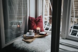 Una vela, un café y un cojín rojo cerca de la ventana de una habitación